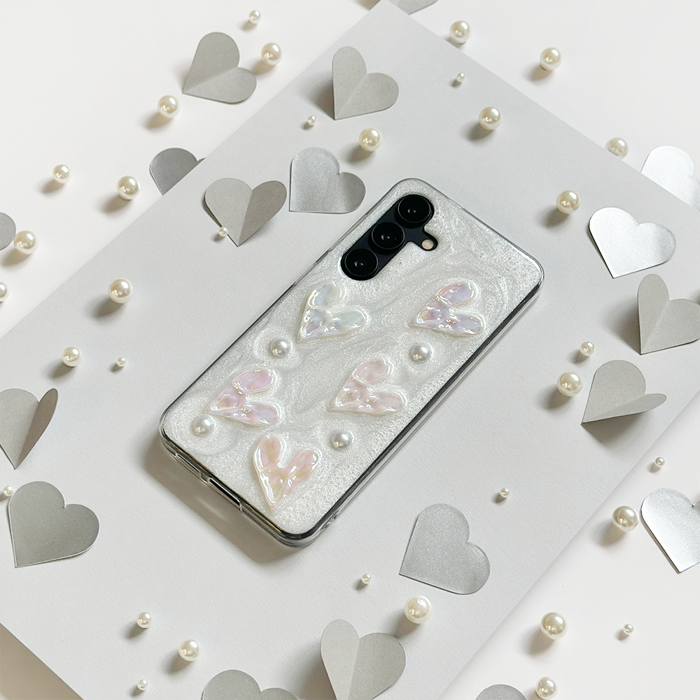 A smartphone with a white case featuring black polka dots and horizontal pink stripes rests on a pink tray.