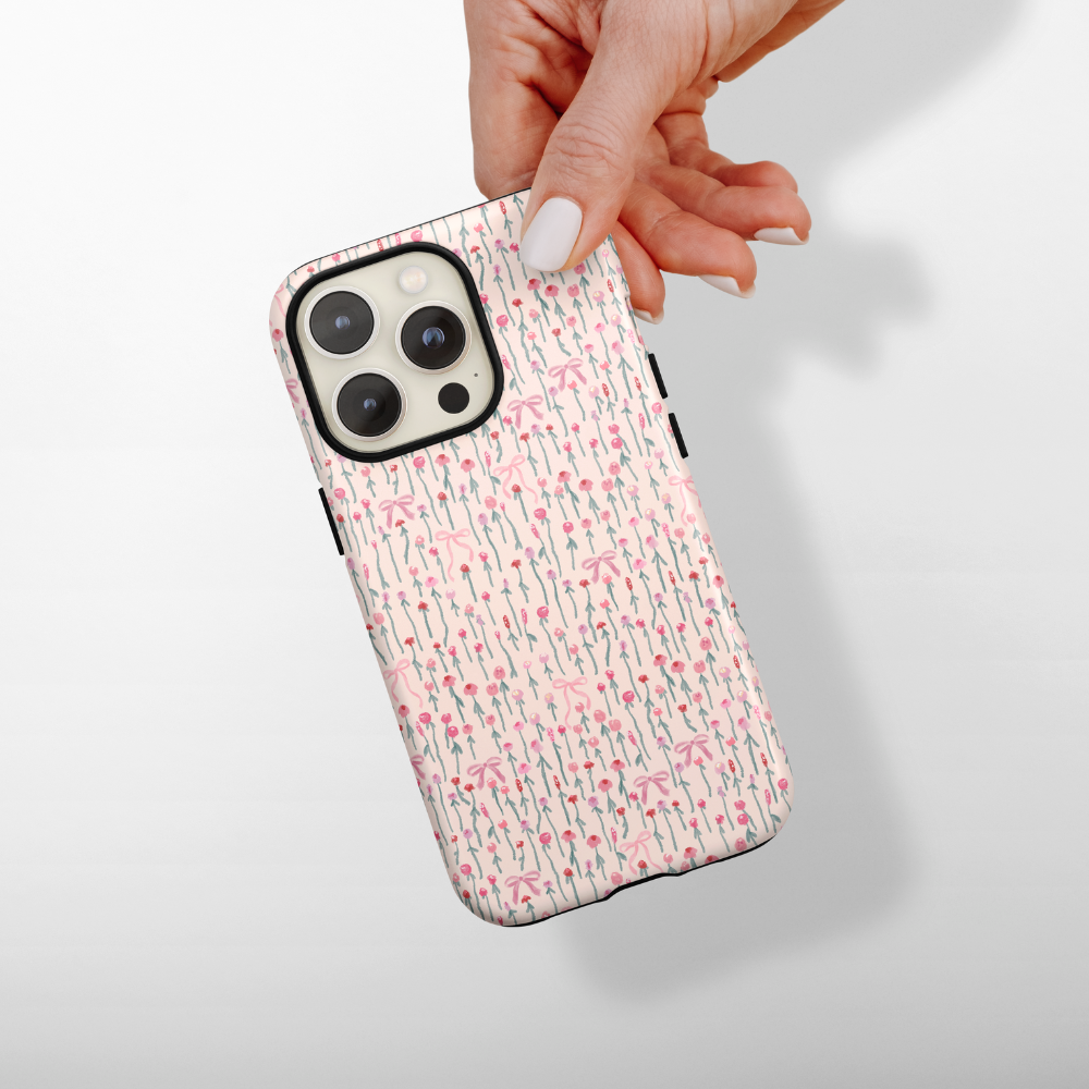 A hand holding a smartphone with a case featuring a pink and white floral pattern, against a light gray background.