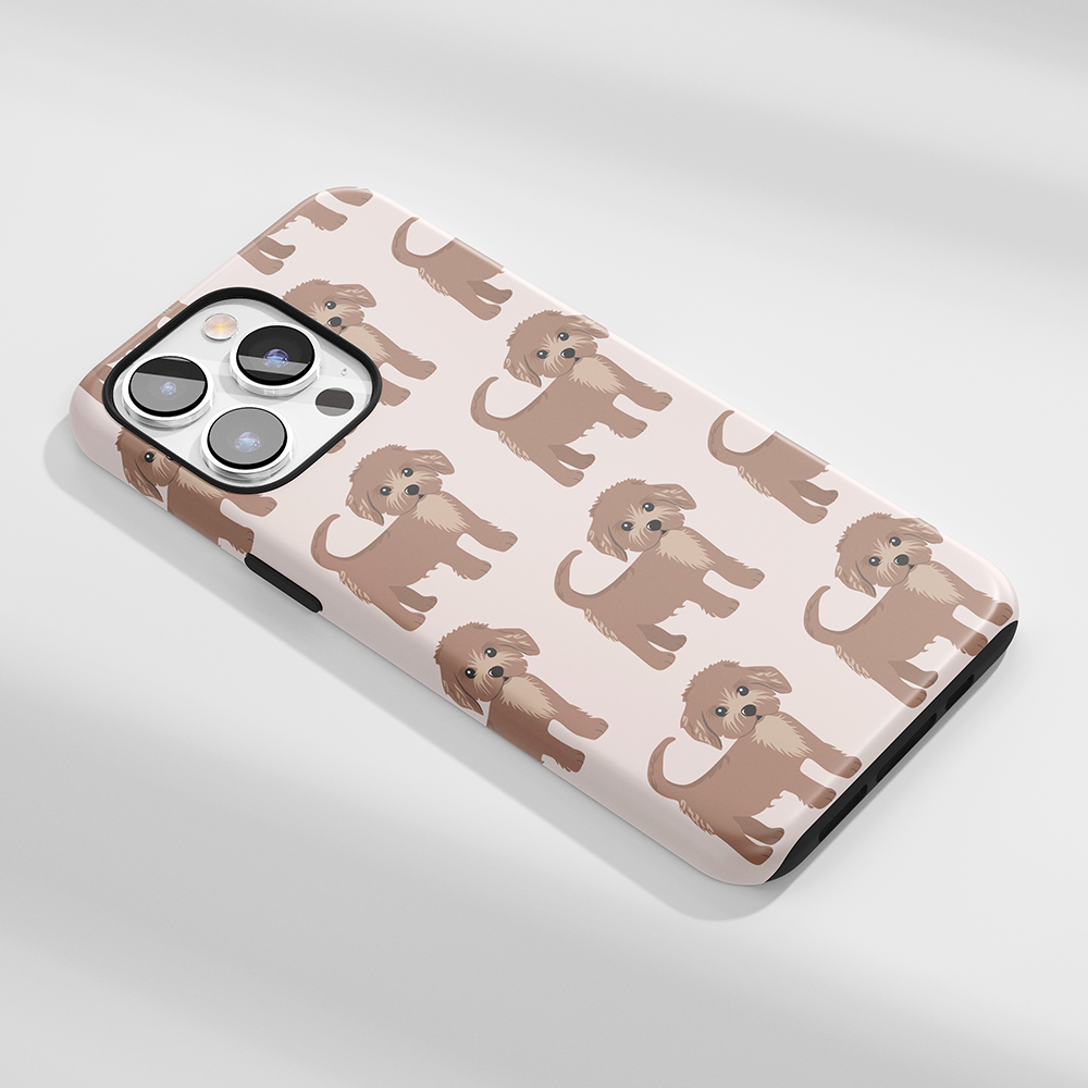 A person holding a smartphone with a case featuring a pattern of cute black and white cartoon beagle dogs against a pink background. The phone is on a wood surface with a box nearby.