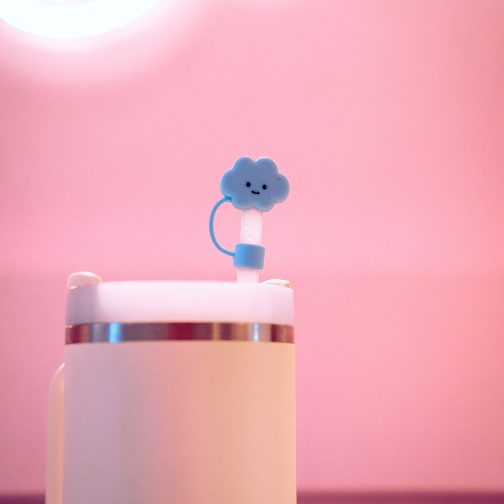 Here's a rewritten version of your sentence using the provided product data:

A close-up of a light pink cup with a blue straw showcasing the Blue Cloud Straw Cover by Coconut Lane, complete with a small, smiling cloud topper at the top. The softly lit background in shades of pink enhances the image's warm and cheerful atmosphere.