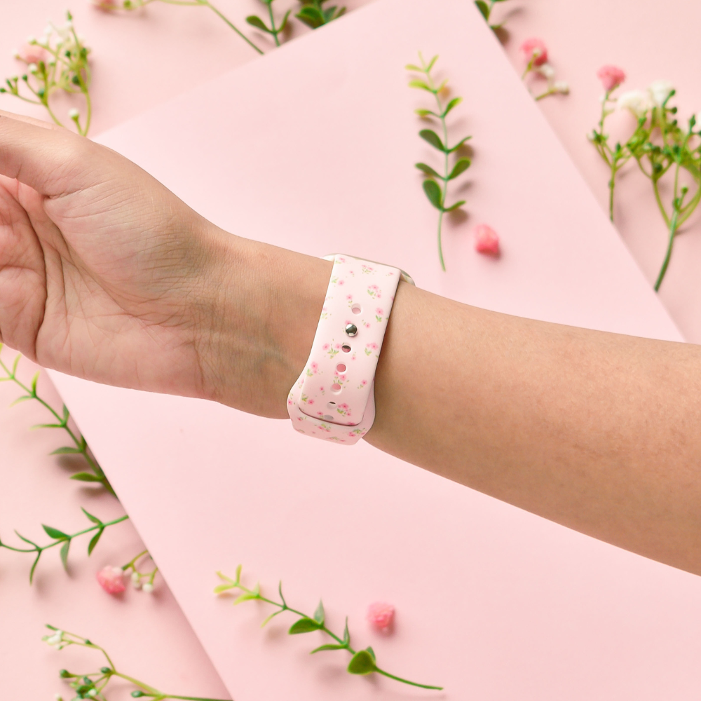 Pink Apple Watch strap with small pink floral pattern on a soft pink background, shown on a wrist.