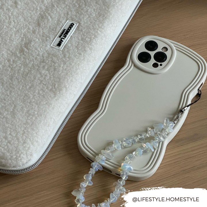 A white, textured laptop sleeve and a lightweight smartphone with a uniquely shaped Coconut Lane NAKD Curvy Phone Case - Vanilla lie on a wooden surface. The phone case features a beaded strap attached. The text "@LIFESTYLE.HOMESTYLE" is written in the bottom-right corner.