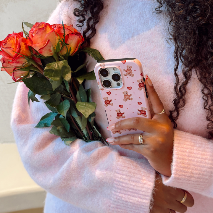 Person holding a bouquet of roses and a phone with a pink case featuring hearts and bears.