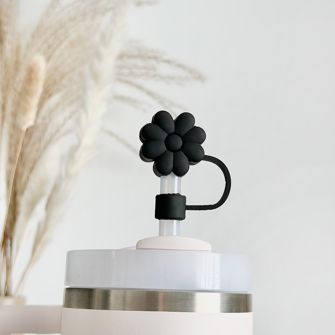 A close-up of a white humidifier featuring the Black Flower Straw Cover from Coconut Lane on top. The background is blurred, showcasing tall, beige pampas grass. The overall aesthetic is minimalistic and clean, highlighting the hygienic design.
