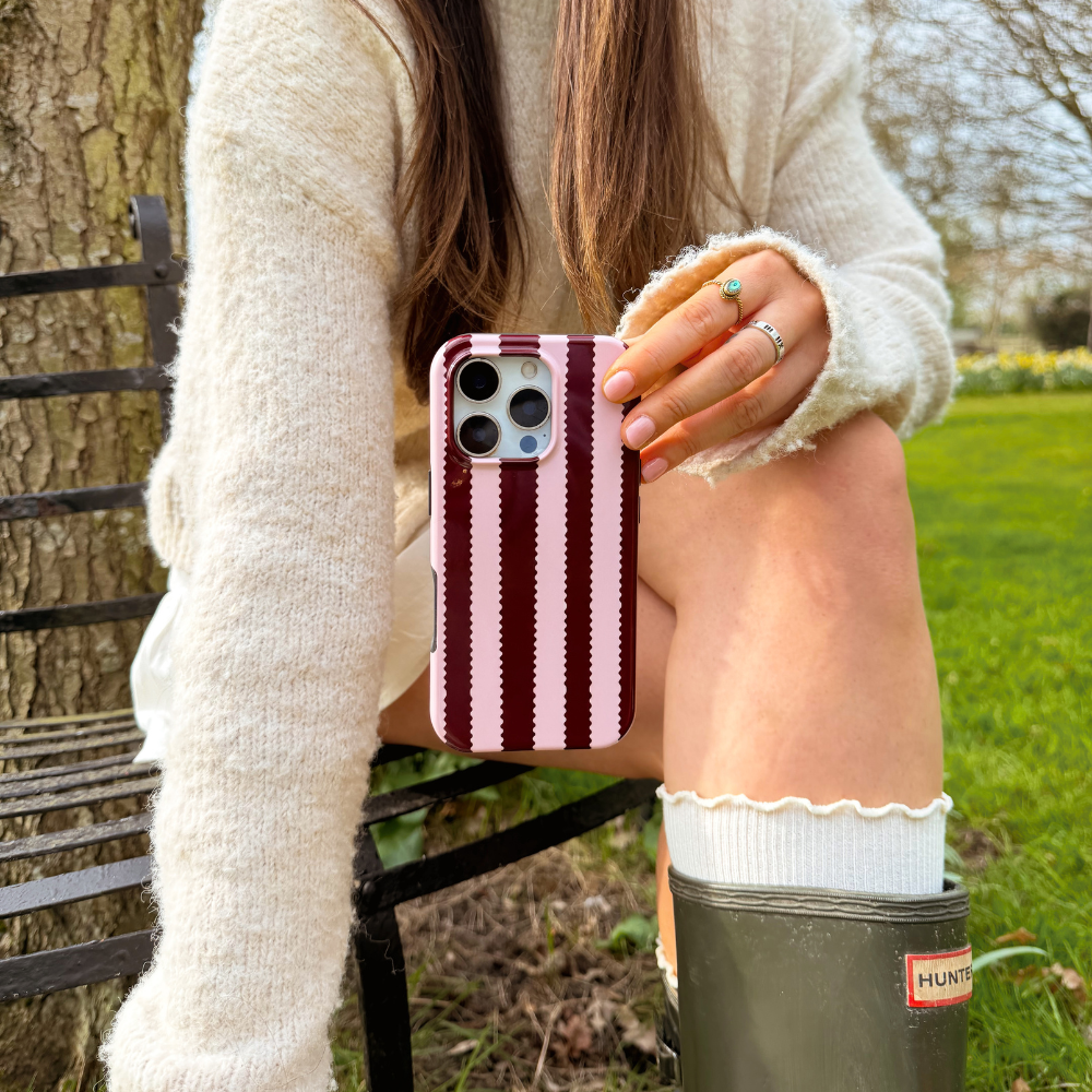 Girl sat in field with blushberry scallop stripes tough phone case in hand wearing cream outfit