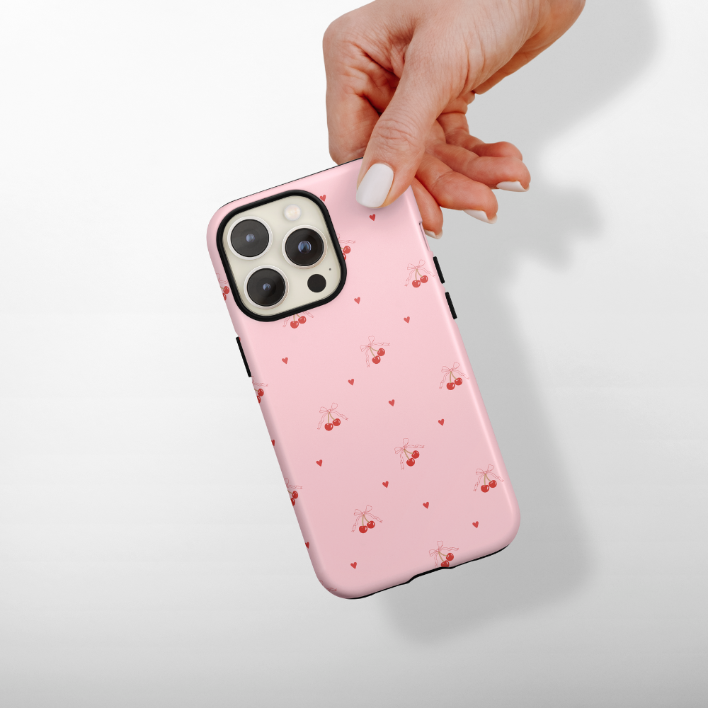 Pink phone case with cherry and heart pattern held by a hand on a light background