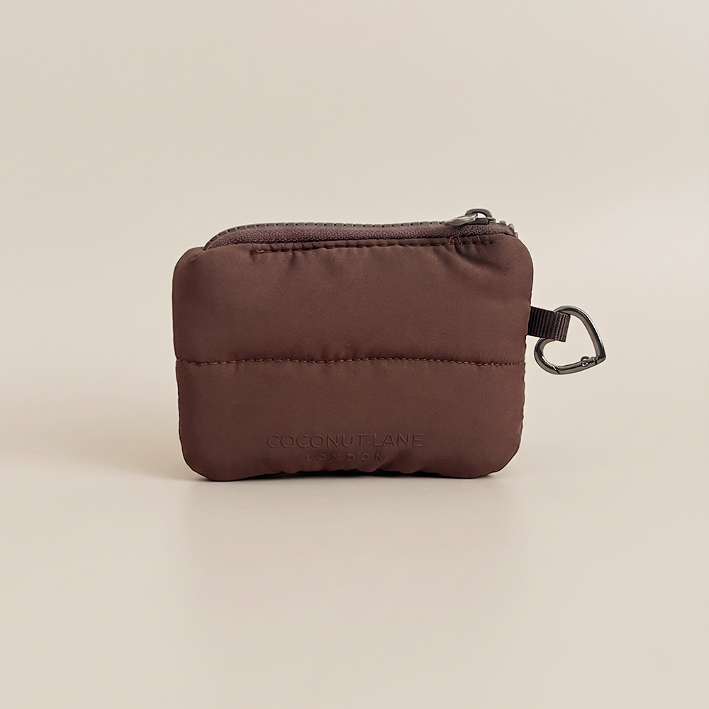 Chocolate brown padded mini keyring bag with zip fastening, silver metal heart shaped clip and embossed Coconut Lane logo on a nude beige background.