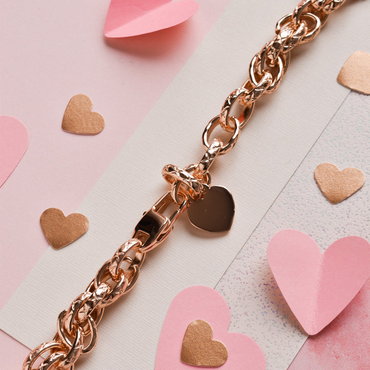 The Chain Bracelet Apple Watch Strap - Rose Gold by Coconut Lane, adorned with a heart-shaped charm, is surrounded by pink and gold paper hearts. The strap, featuring stainless steel metal accents, and the decorations are elegantly displayed on a light pink surface with some white and glitter accents.