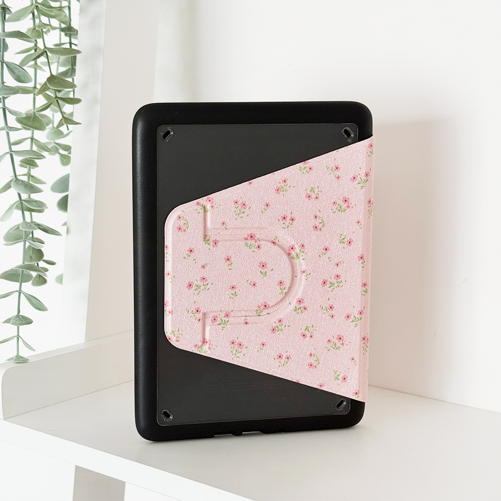 Kindle Paperwhite 11th Gen in a pink floral case stands upright on a white shelf next to a leafy green plant.