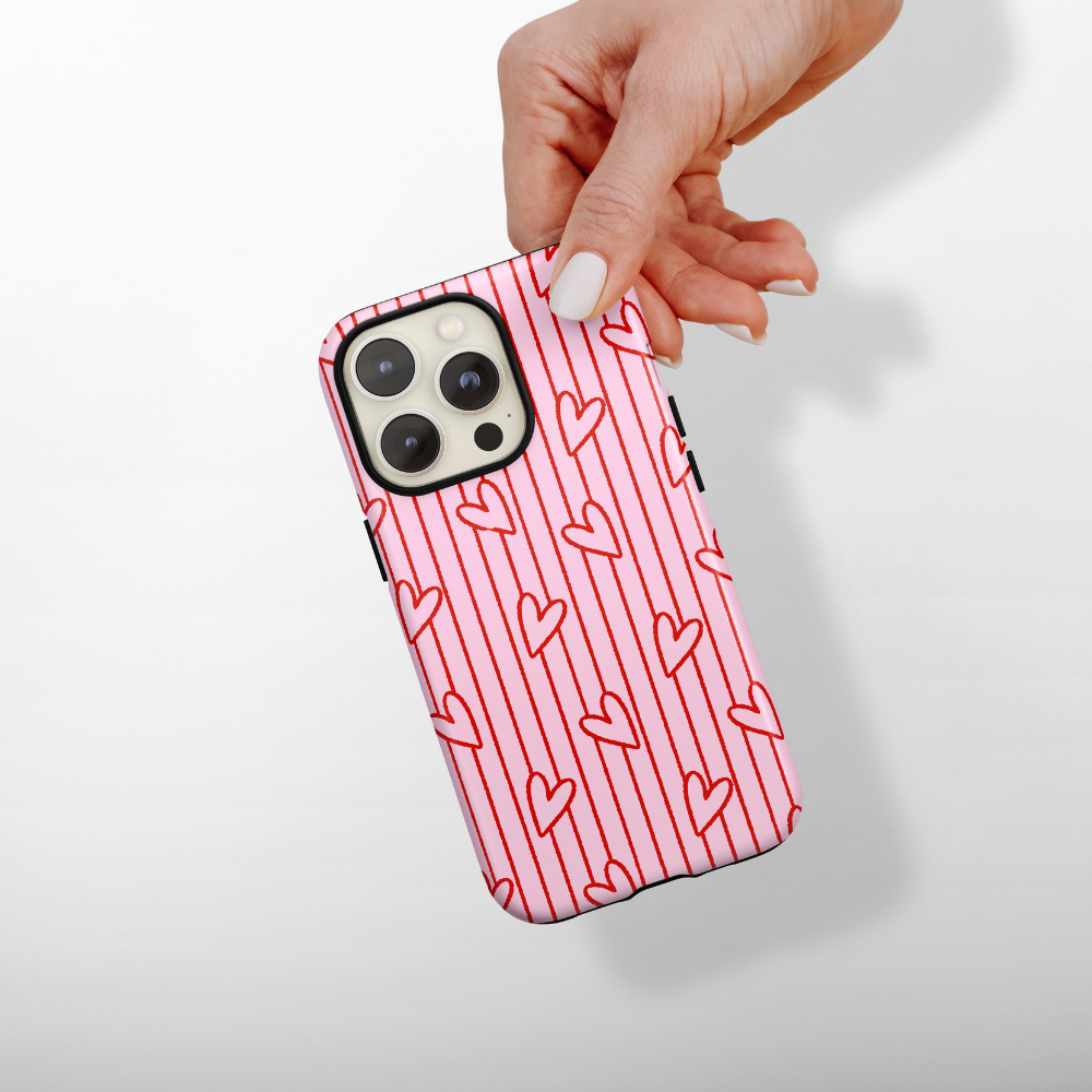 Phone case with a pink and red heart pattern held by a hand on a light background