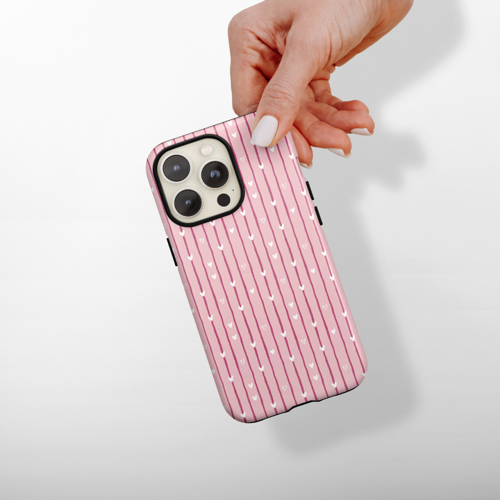 Phone case with pink and white striped pattern with hearts, held by a hand on a light background