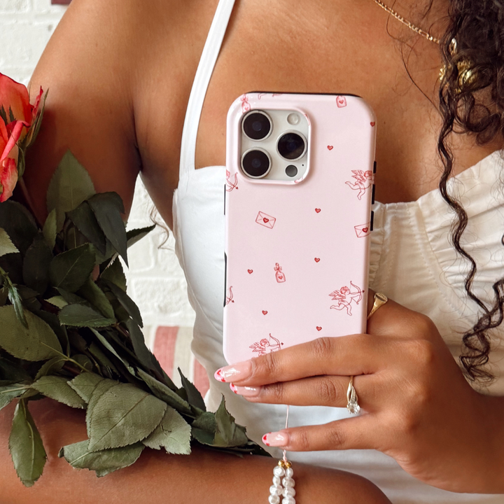 Person holding a phone with a pink case featuring cupid designs, next to roses.
