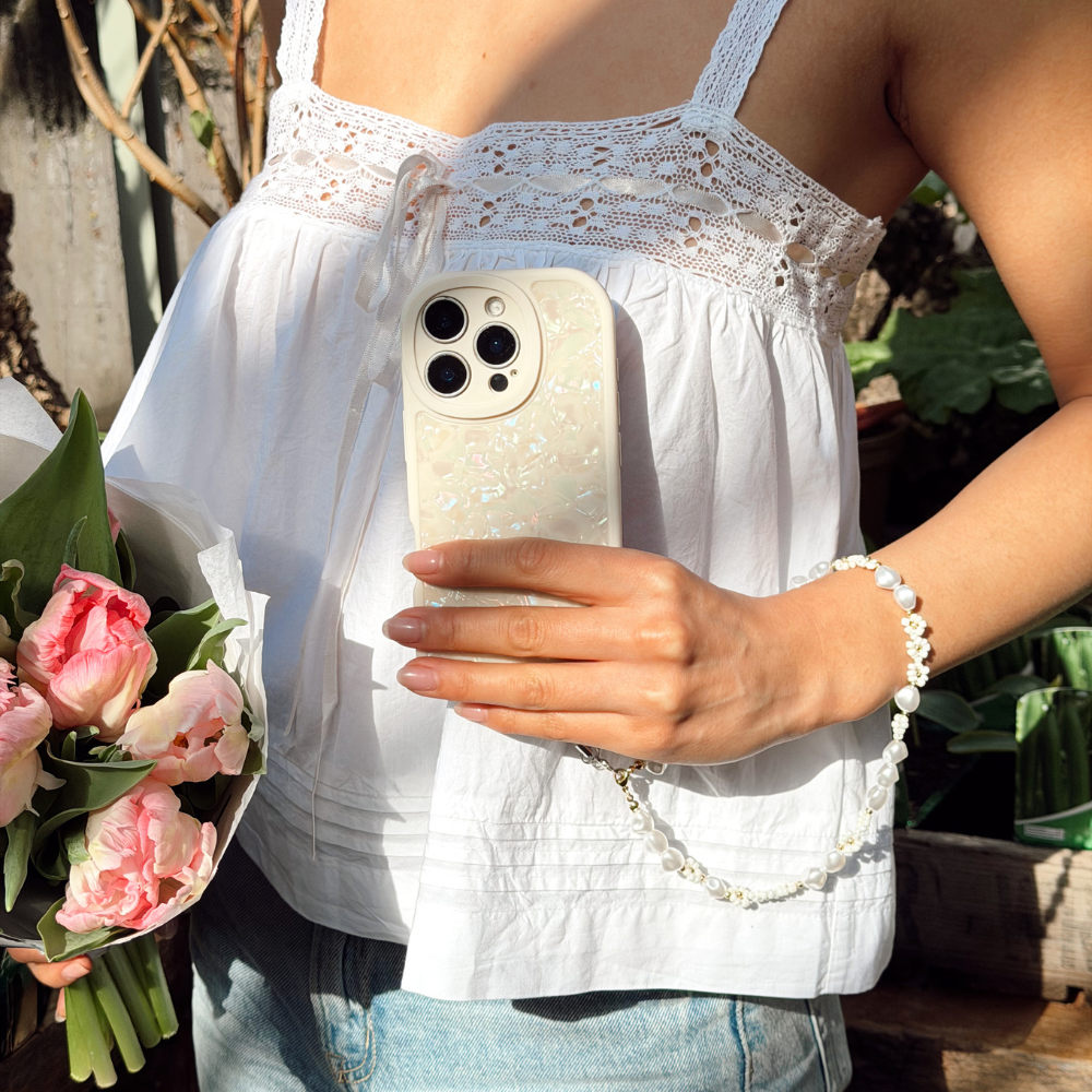 Girl in greenhouse holding flowers posing with her Moonstone Pearl Phone Case that's shining in the sun