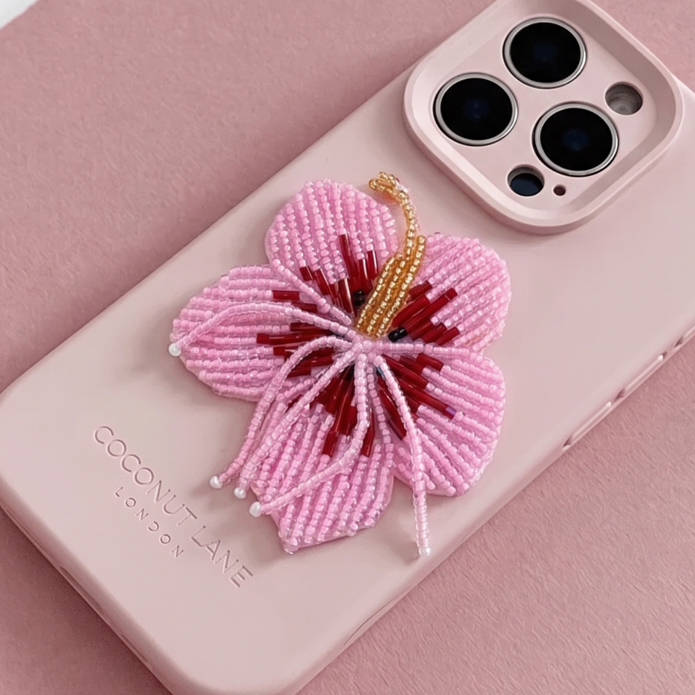 Pink 3D hibiscus flower made from beads and sequins, on top of a pink Coconut Lane Phone Case. 
