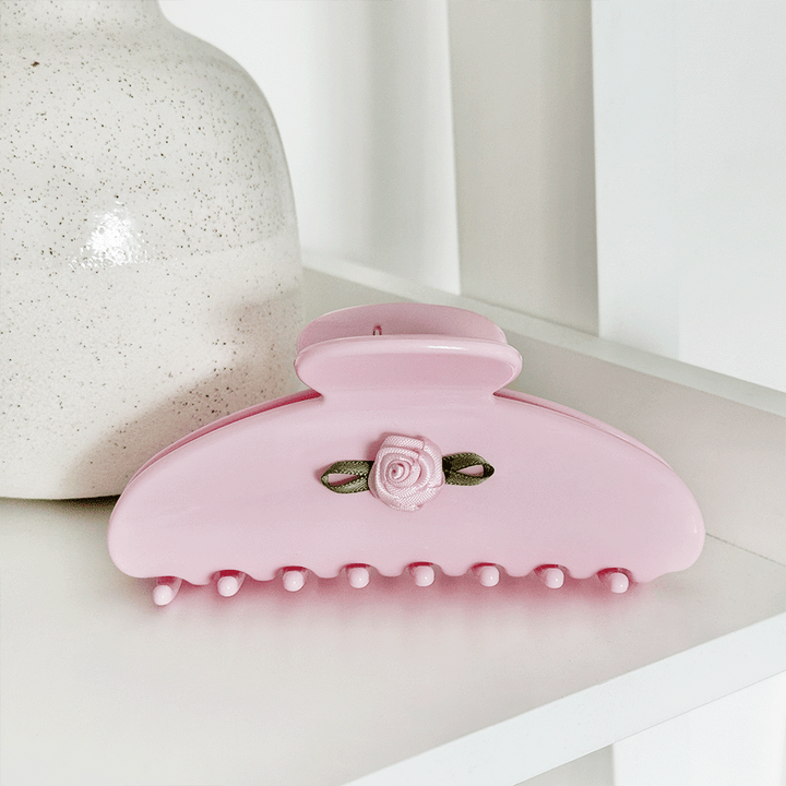 Pink hair claw clip with a small rose embellishment and green ribbon accent.