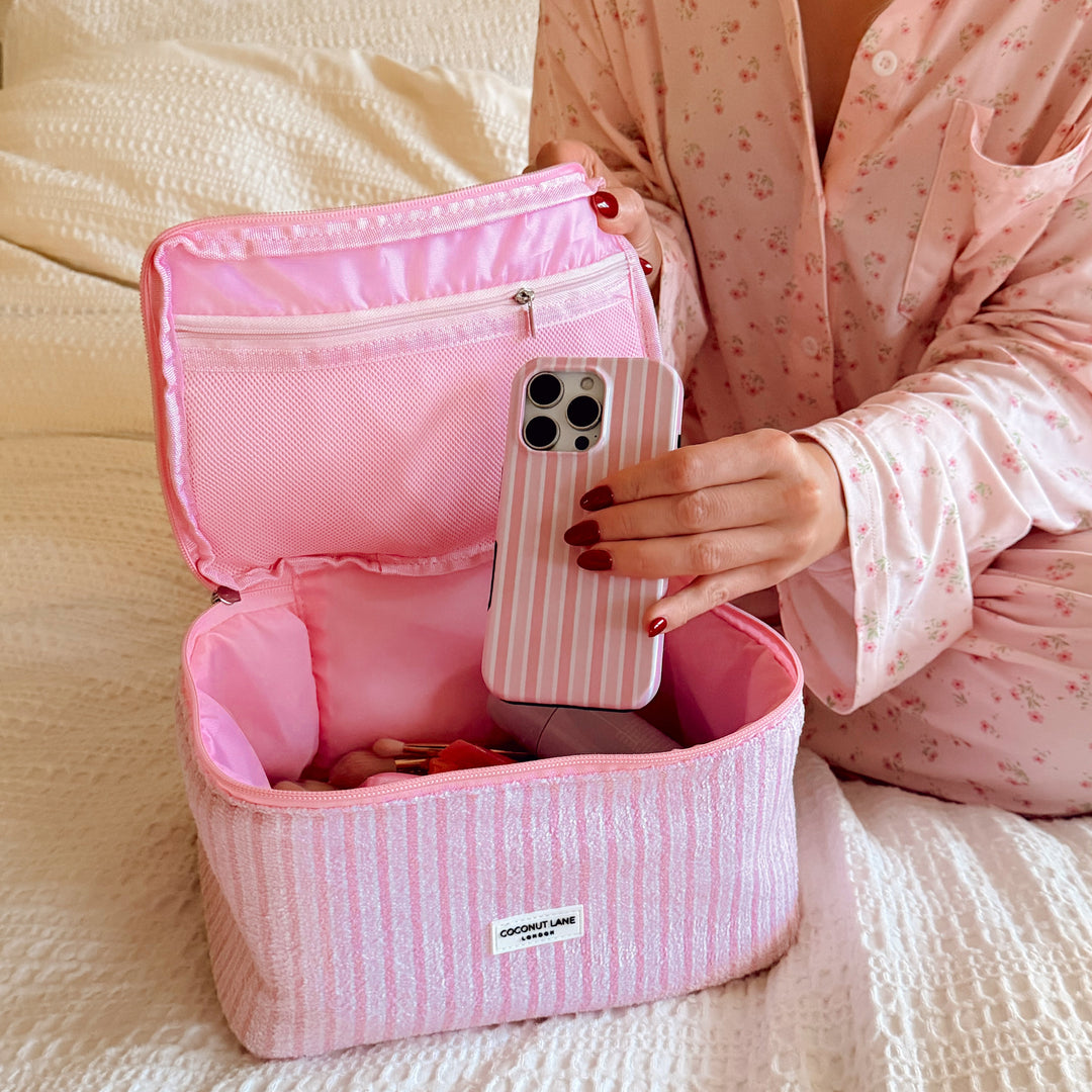 Person holding Powder Stripes Phone case next to an matching vanity bag on a bed.