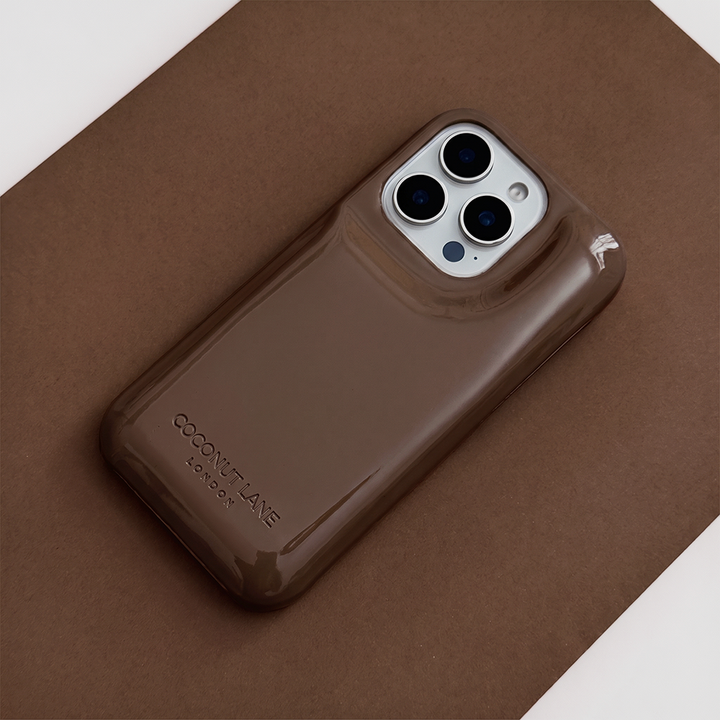 Glossy chocolate brown Coconut Lane puffer phone case with embossed logo, displayed diagonally on a matching brown background.