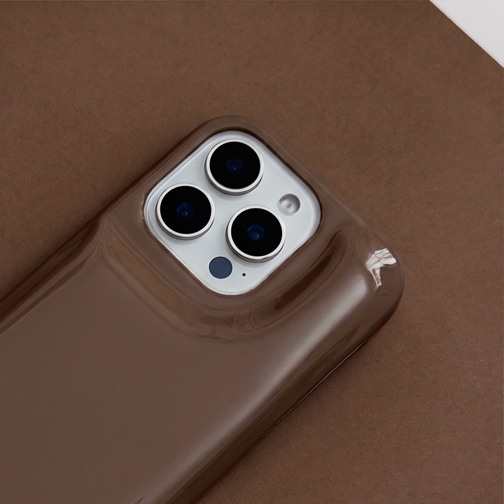 Close-up of glossy chocolate brown Coconut Lane puffer phone case with embossed logo, displayed diagonally on a matching brown background.