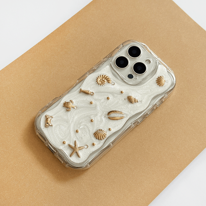 A clear phone case with a white pearlescent background, gold seashell and starfish embellishments, shown on a gold background.
