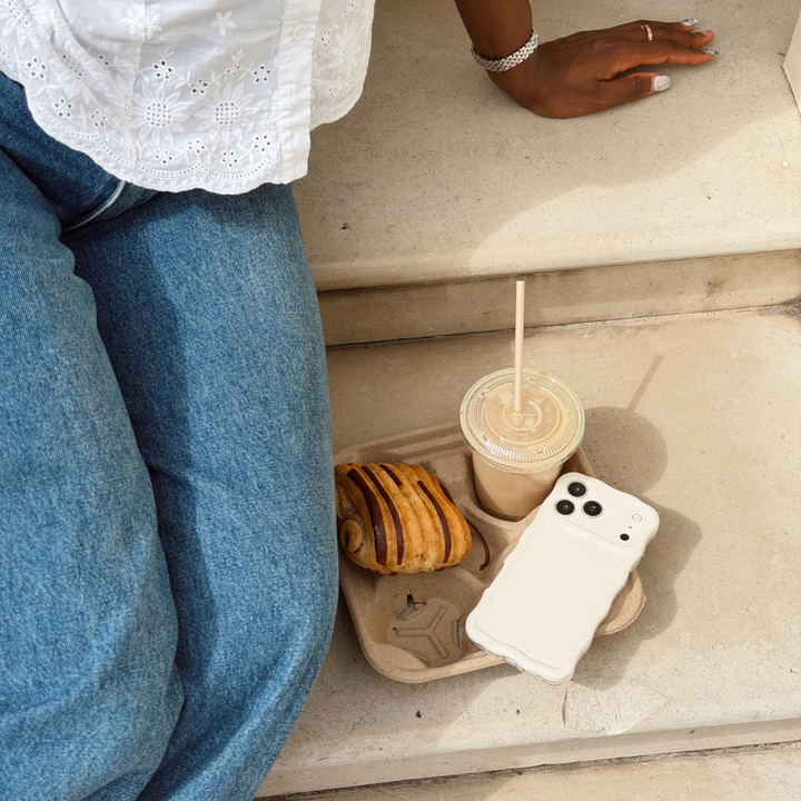 Girl sat on steps with her iced coffee, croissant and her wavy phone case in the shade cloud dancer