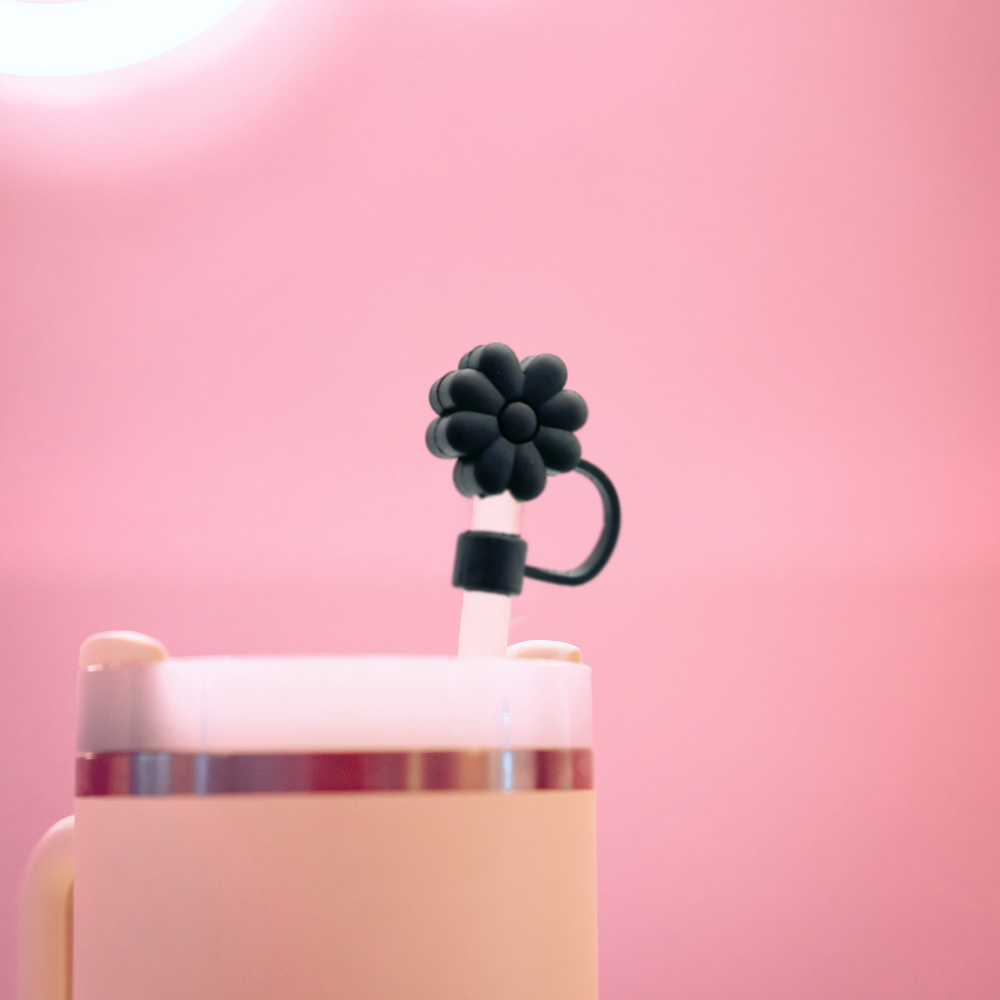 A close-up image of a cream-colored cup with Coconut Lane's Black Flower Straw Cover attached. The background is a gradient of soft pink, giving the photo a whimsical and delicate ambiance while ensuring the setup remains hygienic.