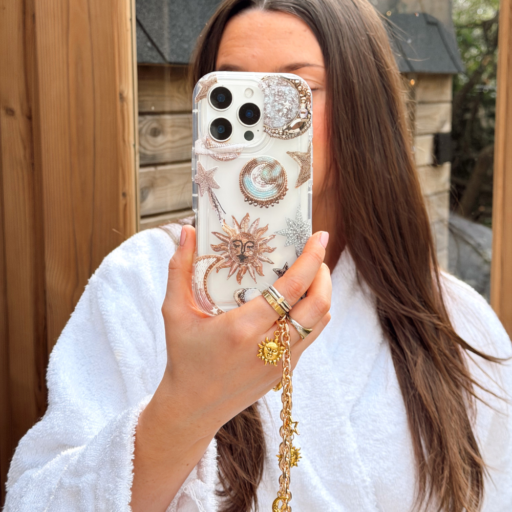 Girl in sauna wearing white dressing gown holding her pastel celestial phone case