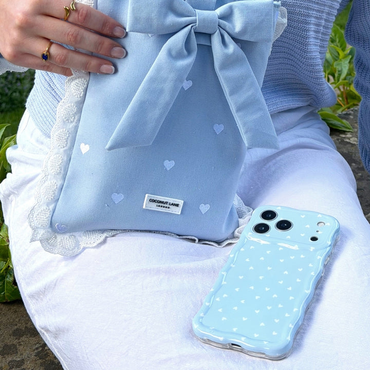 Powder blue hearts book sleeve with a bow and matching phone case on a white skirt.