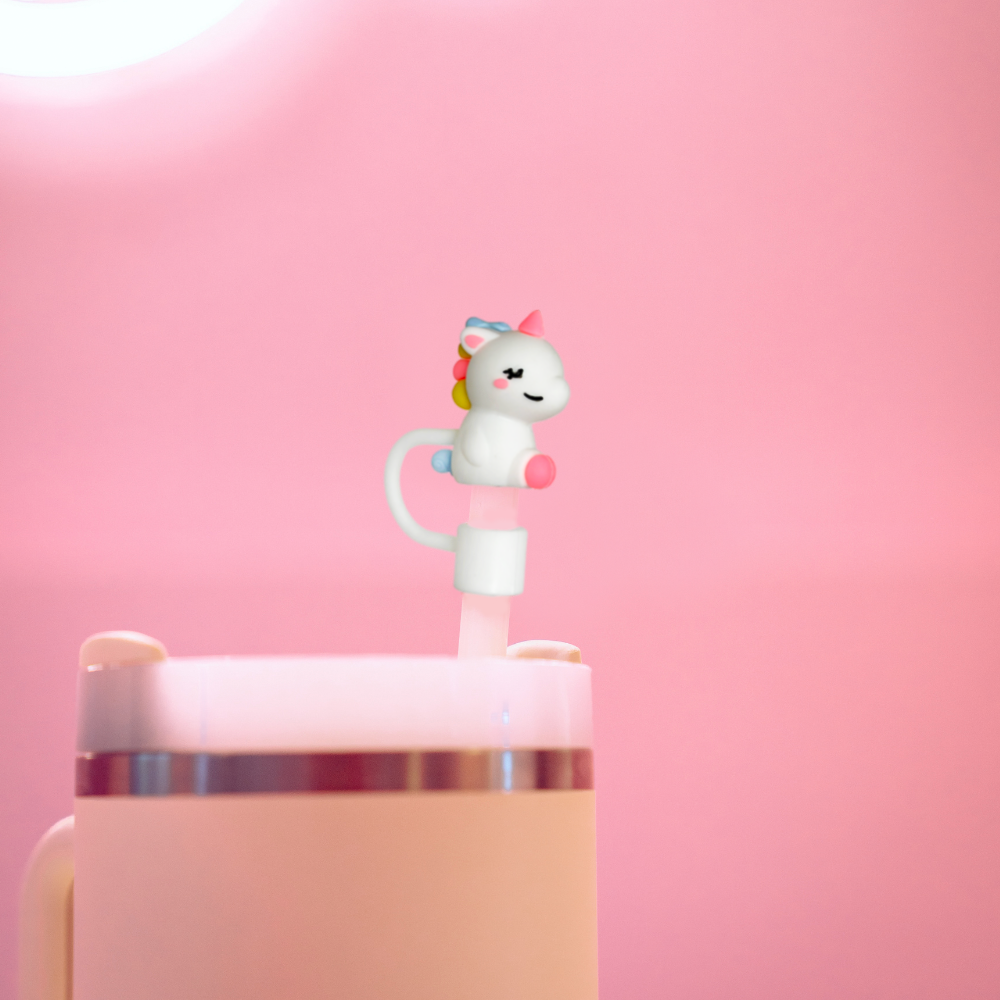 A close-up shot of the Coconut Lane Unicorn Straw Cover, featuring a whimsical white unicorn with a pink mane on top of a pink-colored tumbler. The background is a soft pink, matching the overall pastel theme. Made from high-quality silicone, this flexible design ensures durability while adding a cute and playful touch.