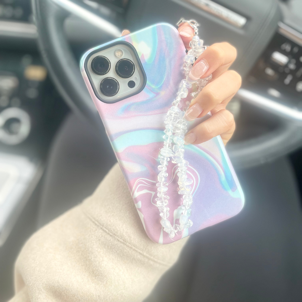 Hand holding Coconut Lane pastel marble phone case with a moonstone crystal strap, inside a car.